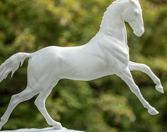 Puede incluir: Una escultura de caballo de porcelana blanca en una pose de carrera. El caballo está sobre una base blanca y se coloca sobre un fondo verde.