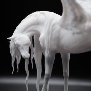 以下が含まれることがあります： 頭を下げた白い翼のある馬、またはペガサスの彫刻。 彫刻は流れるようなたてがみと尾のディテールを持ち、翼は部分的に見えます。 背景は黒です。
