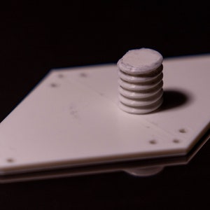 Puede incluir: Una placa de pl&aacute;stico blanca en forma de diamante con varios agujeros y un tornillo de pl&aacute;stico blanco roscado en el centro.