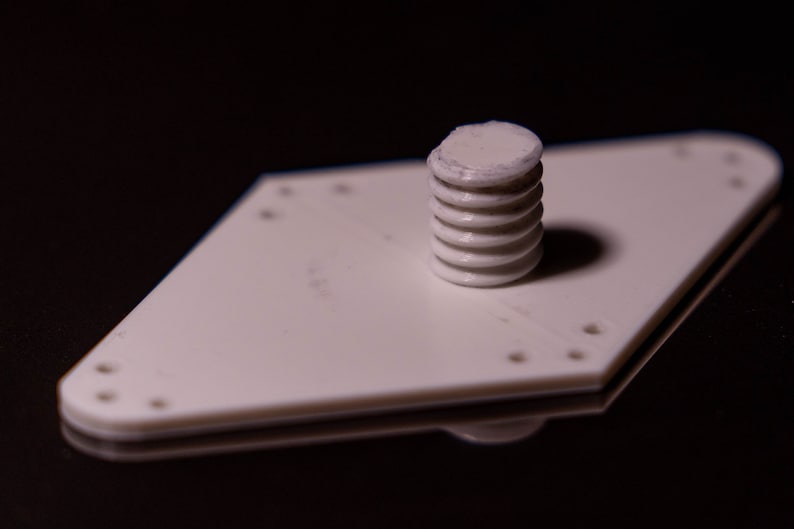 Puede incluir: Una placa de pl&aacute;stico blanca en forma de diamante con varios agujeros y un tornillo de pl&aacute;stico blanco roscado en el centro.