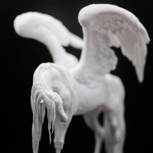 以下が含まれることがあります： 黒い背景に、白いペガサスの彫刻。彫刻は、詳細な翼と流れるようなたてがみと尾を持っています。馬は立っていて、頭をわずかに下げています。