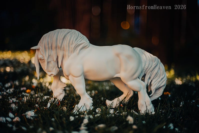 May include: A white horse sculpture with a flowing mane and tail, standing in a grassy area with small white petals. The sculpture has a detailed, realistic appearance. The text "HornsfromHeaven 2026" is visible in the upper right corner.