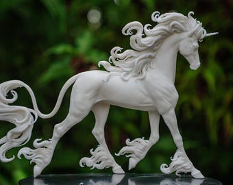 Puede incluir: Una escultura de unicornio blanco con melena y cola fluidas, y un solo cuerno. La escultura está detallada con rizos intrincados y una pose dinámica, sobre un fondo verde borroso.