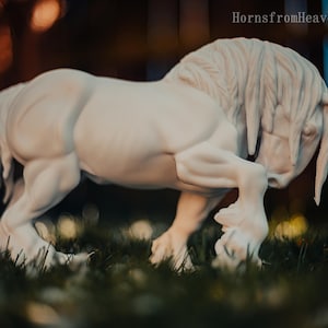 May include: A white sculpture of a horse in a dynamic pose, with its head lowered and front leg bent. The horse has a flowing mane and tail, and is set against a blurred background of green grass and bokeh lights. The text "HornsfromHeaven 2026" is visible.