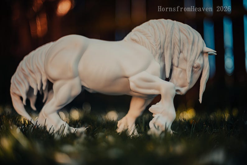 May include: A white sculpture of a horse in a dynamic pose, with its head lowered and front leg bent. The horse has a flowing mane and tail, and is set against a blurred background of green grass and bokeh lights. The text "HornsfromHeaven 2026" is visible.
