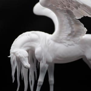 以下が含まれることがあります： 黒い背景に、白い翼のある馬、ペガサスの彫刻。 馬の頭は下がり、長いタテガミが流れ落ちています。 翼は羽毛のテクスチャで詳細に表現されています。