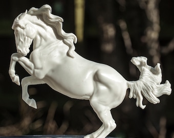 May include: A white ceramic sculpture of a horse rearing up on its hind legs. The horse has a long flowing mane and tail.