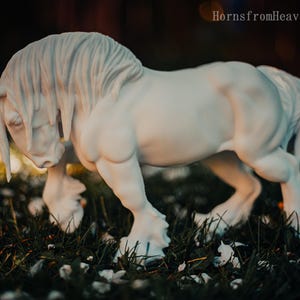May include: A white horse sculpture with a flowing mane and tail, standing in a grassy area. The horse is sculpted with detailed musculature and is captured in a dynamic pose. The image has a soft focus background with the text "HornsfromHeaven 2026".