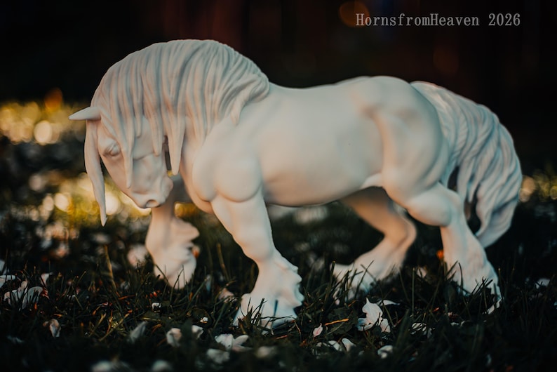 May include: A white horse sculpture with a flowing mane and tail, standing in a grassy area. The horse is sculpted with detailed musculature and is captured in a dynamic pose. The image has a soft focus background with the text "HornsfromHeaven 2026".