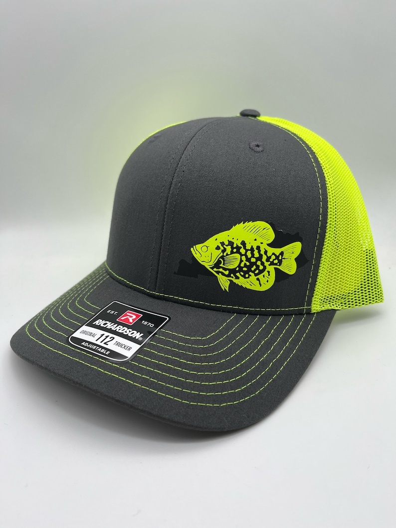 May include: A gray Richardson 112 trucker hat with a neon green fish graphic. The hat features a neon green mesh back and brim stitching. The front panel displays the Richardson logo and "Original 112 Trucker" text.