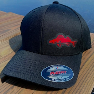 May include: Black Flexfit baseball cap with a red fish graphic on the front. The cap has a curved brim and a small button on top. The Flexfit logo and text "IT FITS YOUR LIFE" are on a sticker on the brim.