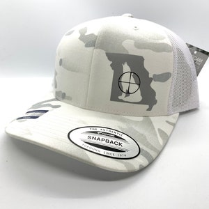 Pode incluir: Bon&eacute; de caminhoneiro branco camuflado com um contorno branco do estado do Missouri com um s&iacute;mbolo de alvo no interior. O bon&eacute; tem uma etiqueta preta "Yupoong The Authentic Snapback Yupoong Since 1974" na parte inferior da aba.