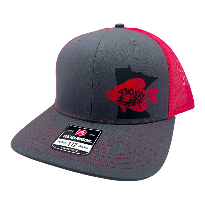 May include: A gray and red trucker hat with a fish graphic. The hat features a red fish design over a black outline of the state of Minnesota. The brim and mesh backing are red, and the hat has the text "RICHARDSON" on a tag.
