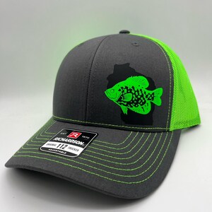 May include: A gray Richardson 112 trucker hat with a neon green fish graphic. The hat features a neon green mesh back, brim, and stitching. The front of the hat has a black outline of a fish with a neon green fish inside.