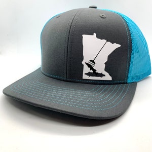 May include: A grey and turquoise trucker hat with a white outline of the state of Minnesota and a fishing lure inside the state. The hat has a mesh back.