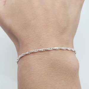 May include: A silver bracelet with a twisted chain design and small beads.