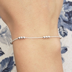 May include: A delicate silver chain bracelet with small round beads. The bracelet is simple and elegant, perfect for everyday wear.