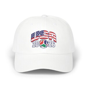 May include: A white baseball cap featuring an embroidered graphic on the front. The design displays the text USA in a red, white, and blue flag pattern, positioned above the numbers 20 and 26 with a colorful, swirling soccer ball icon in between.