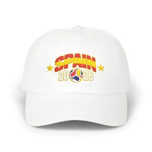 May include: A white baseball cap featuring embroidered text that reads SPAIN 2026 in red and yellow colors. A stylized soccer ball graphic sits between the numbers, flanked by two yellow stars on either side of the text on the front panel.