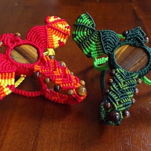 May include: Two macrame wall hangings with a wooden circle in the center. One is red and yellow, the other is green.