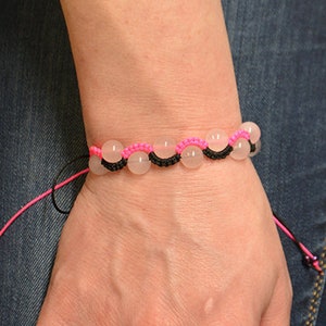 Puede incluir: Un brazalete con cuentas transparentes y cuerda rosa y negra.