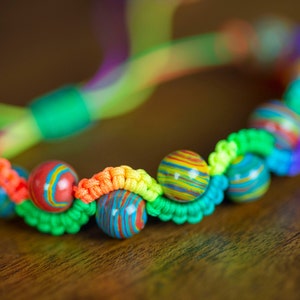 Puede incluir: Un brazalete colorido con hilo verde, naranja y amarillo tejido a través de cuentas de piedra multicolor.