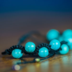 May include: A turquoise beaded bracelet with black cord. The beads are round and have a slightly irregular surface.