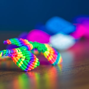 May include: A colorful rainbow friendship bracelet made of woven string. The bracelet is in the shape of a figure eight with two loops.