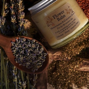 Könnte beinhalten: Ein Glasgefäß mit Flower Balm, einem silbernen Deckel und einem beigen Etikett mit der Aufschrift Flower Balm, Moisturising & Cleansing Balm, For dry & sensitive skin, A rich, nourishing multi-use balm to sooth & protect dry skin, Calendula - Honey - Immortal Flower.