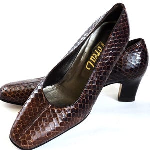 Peut inclure: Escarpins en cuir marron avec un motif peau de serpent. Les chaussures ont un petit talon et un bout arrondi. Le mot "Loreal" est imprimé en or sur la semelle intérieure. Les talons mesurent environ 5 cm.