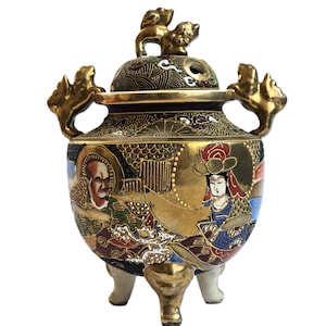 Può includere: Un bruciatore di incenso giapponese vintage con finitura dorata, con opere d'arte dettagliate di figure e motivi. Il bruciatore ha un coperchio con due piccole figure di leone e manici ornati. La base ha tre piedini bianchi.