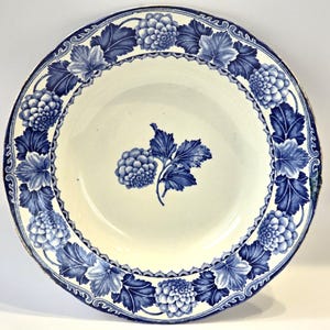 May include: A round, antique ceramic plate with a cream-colored center and a blue floral design. The border features alternating blue flowers and leaves. A cluster of blue flowers and leaves is in the center of the plate.