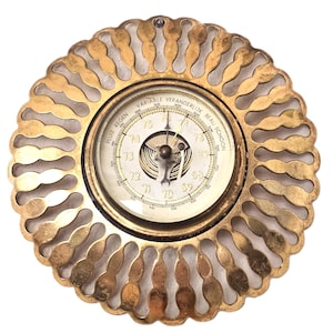 May include: Vintage brass barometer with a circular dial and a decorative, scalloped edge. The face shows pressure readings and the words "Variable Veranderlijk Beau Schoon" and "Pluie Regen". A classic weather instrument.