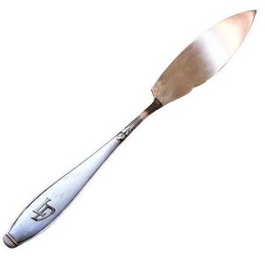 May include: A silver butter knife with a pointed tip and a decorative handle. The handle has a small engraved letter 'D' on it.