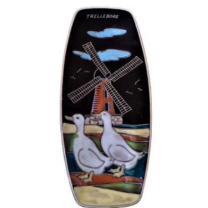 Puede incluir: Un plato de servir de cerámica con fondo negro y una escena colorida de un molino de viento, dos patos y un cielo azul. El plato es de forma ovalada y tiene la palabra "Trelleborg" escrita en la parte superior.