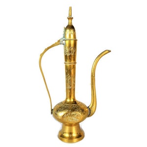 Puede incluir: Una jarra de metal dorado con intrincados diseños florales. La jarra tiene un pico largo y curvo y un asa.