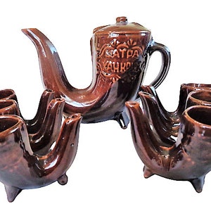 Könnte beinhalten: Eine braune Teekanne aus Keramik und sechs passende Tassen in Hornform. Die Teekanne trägt den Text "Ватра" und "Захр" an der Seite.