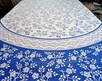 May include: A round white tablecloth with a blue floral pattern. The center of the tablecloth has a white background with blue flowers and leaves. The outer edge of the tablecloth has a blue background with white flowers and leaves.