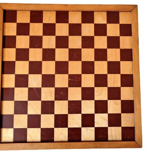 May include: A wooden chessboard with a brown and tan checkered pattern. The board is surrounded by a wooden frame.