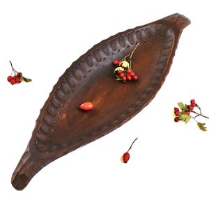 Puede incluir: Una bandeja de servir de madera marrón oscuro con un diseño tallado alrededor del borde. La bandeja tiene forma de hoja y tiene un asa ligeramente curvada.