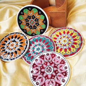 May include: Set of five colorful ceramic coasters with intricate geometric patterns. The coasters feature a variety of colors, including red, yellow, green, blue, and black. They are perfect for adding a touch of style to any home.