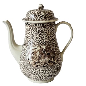 Puede incluir: Una cafetera de cerámica marrón y blanca con un diseño floral y un pájaro. La cafetera tiene un esmalte craquelado marrón.