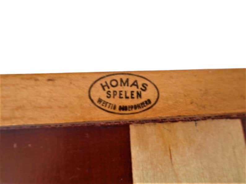 May include: Close-up of a wooden game board with a brown and white checkered pattern. The board has a label that reads "Homas Spelen" in a black oval.