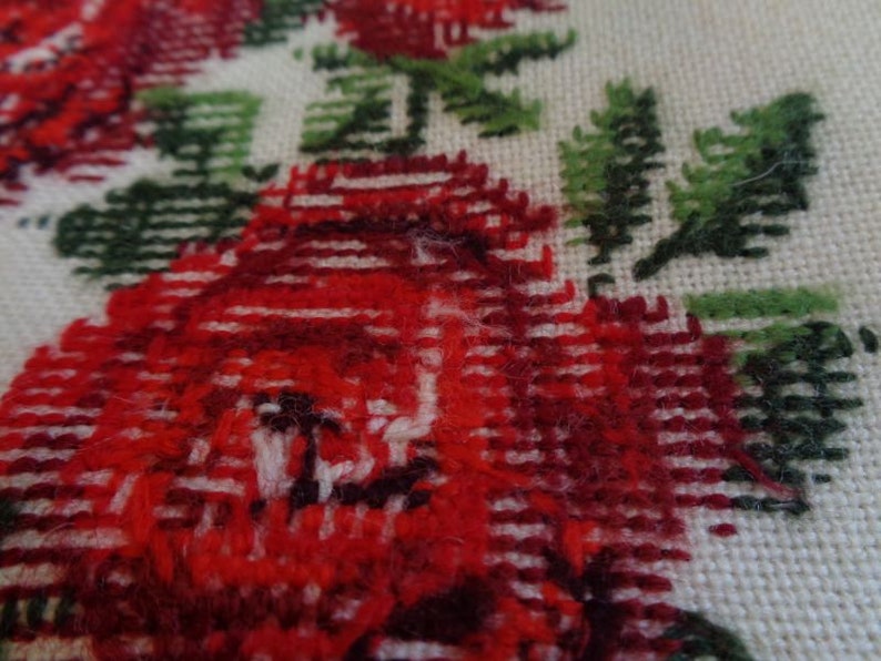 May include: Close-up of a red and green embroidered fabric with a floral design. The fabric is woven with a textured pattern and features a repeating motif of red roses and green leaves.