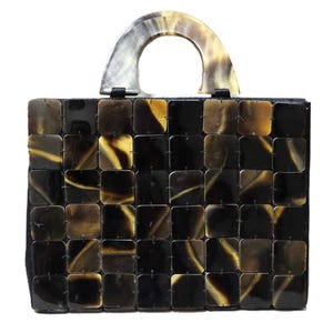 Puede incluir: Un bolso negro con asa de cuerno. El bolso está hecho de un mosaico de pequeñas piezas cuadradas marrones y negras.