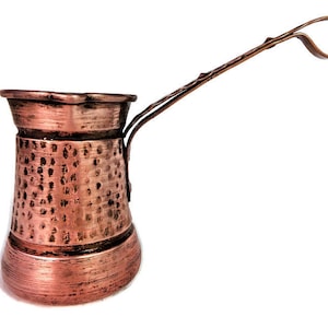 Op de afbeelding: Een Turkse koffiepot van koper met een gehamerde afwerking en een lange, gebogen handvat.