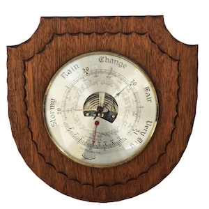 May include: A vintage barometer with a wooden frame. The circular gauge features a silver face with a needle indicating atmospheric pressure. The words "Rain", "Change", "Fair", and "Very Dry" are visible. A thermometer is also included.