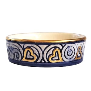 Peut inclure: Un petit bol rond en céramique bleu et blanc avec un bord doré et des motifs de cœurs dorés. Le bol est parfait pour contenir de petits objets comme des bijoux ou des bibelots.