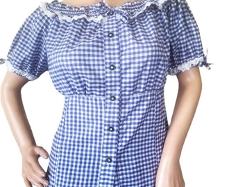 Puede incluir: Una blusa de botones de cuadros azules y blancos con un ribete de encaje blanco alrededor del cuello y las mangas. La blusa tiene una cintura ajustada y mangas cortas.