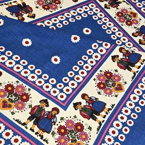 May include: Blue fabric with a white and red daisy pattern. The fabric has a white border with a pink and red trim. The border features a repeating pattern of flowers and people in traditional clothing.